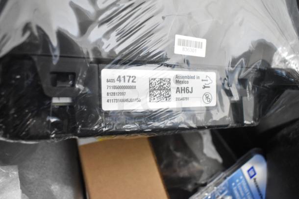 Brand new automotive parts including GMC emblems and GM wheel locks in a black poly bin. Label shows "Assembled in Mexico."