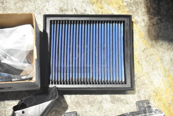 Brand new lot of car parts, including GMC emblems and GM wheel locks, in a black poly bin.