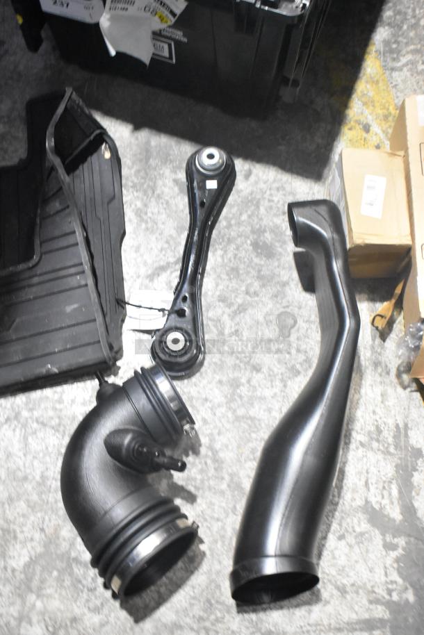 Brand new car parts lot with black car mats, hose, and suspension arm. Included in black poly bin.