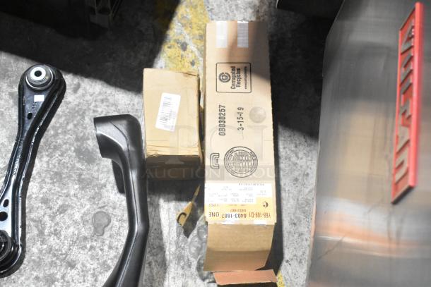 Lot of various car parts and boxes on floor, including control arms and boxed items with shipping labels, in black poly bin.