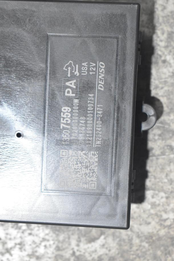 Black poly bin containing brand new GM 25958214 tail lamp assembly and various car parts. Denso label visible.