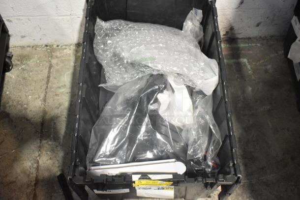Black poly bin filled with brand new car parts, including spark plugs and a grille, wrapped in plastic and bubble wrap.