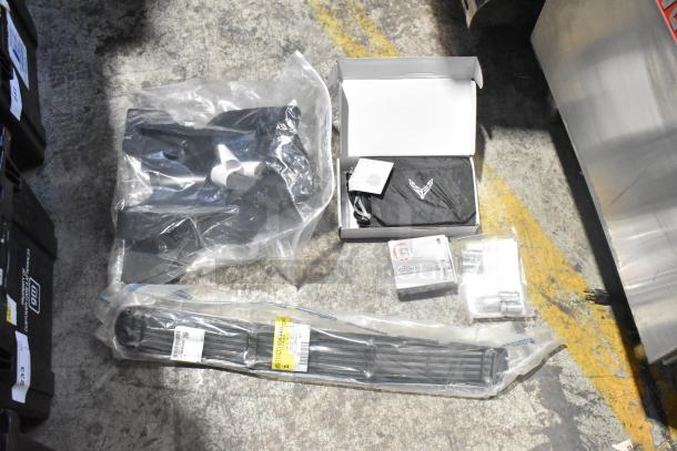 Lot of brand new car parts including spark plugs, black grille, and assorted items in packaging on floor; labels visible.