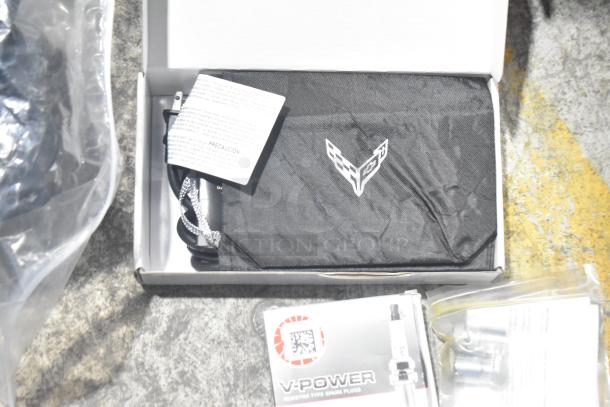 Lot of various new car parts, including spark plugs and components in a black poly bin with Corvette logo.
