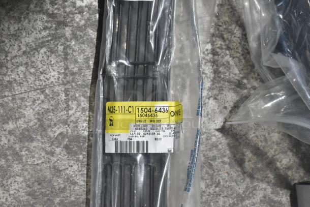 Brand new car parts in black poly bin, including labeled grille with tag "M35-111-C1" and spark plugs.