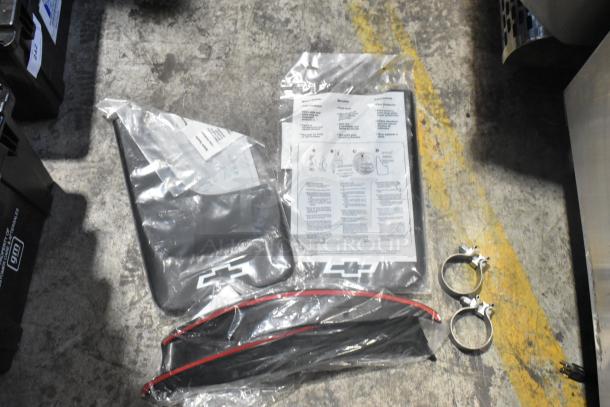 Brand new car parts in black poly bin, including Chevrolet-branded items, instructions, and metal clamps. Ideal for collectors or repairs.