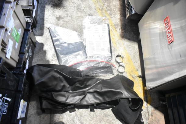 Brand new car parts in black poly bin, including black fabric material, metal clamps, and labeled plastic bags with instructions.