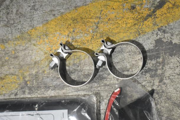 Brand new lot of various car parts in a black poly bin, including metal clamps and sealed accessories.