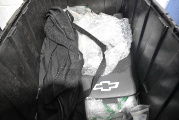 Black poly bin with brand new car parts, including a Camaro bag with a Chevrolet logo, wrapped in bubble wrap.
