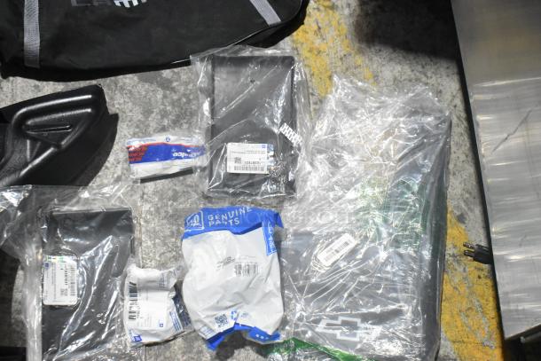 Brand new lot of various car parts in original packaging, including a Camaro bag, displayed within a black poly bin.