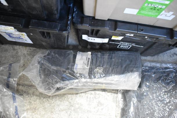 Brand new car parts in black poly bin, includes spark plugs and grille. GM label visible, unopened packaging.