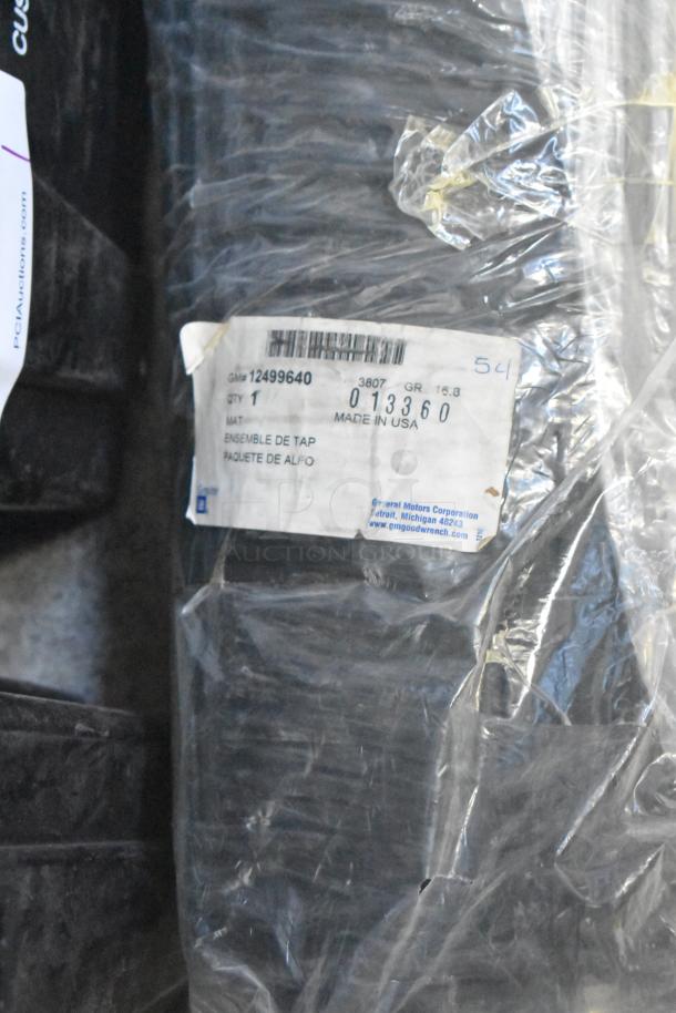 Brand new car parts lot with spark plugs, black grille in poly bin, label shows GM part #12499640, made in USA.