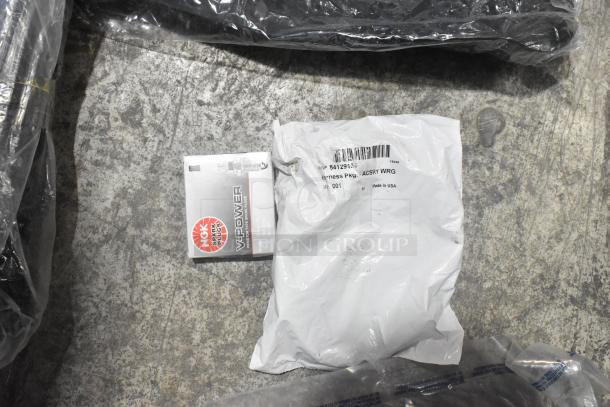 Lot of brand new car parts including NGK spark plugs, wiring harness in bags, all in black poly bin.