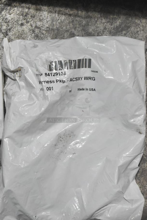 White plastic bag labeled "Harness Pkg. ACSRY WRG", P/N# 84129138, Made in USA, slightly dirty, on concrete surface.