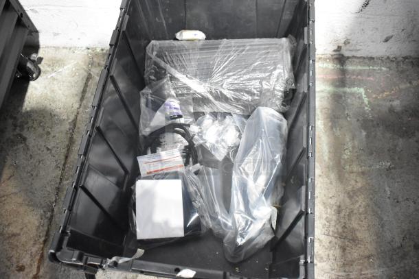 Lot of new car parts including spark plugs and a grille, packed in a black poly bin, with visible packaging and labels.