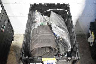 Black poly bin containing a lot of various brand new car parts including black car mats, wrapped cables, and pipe.