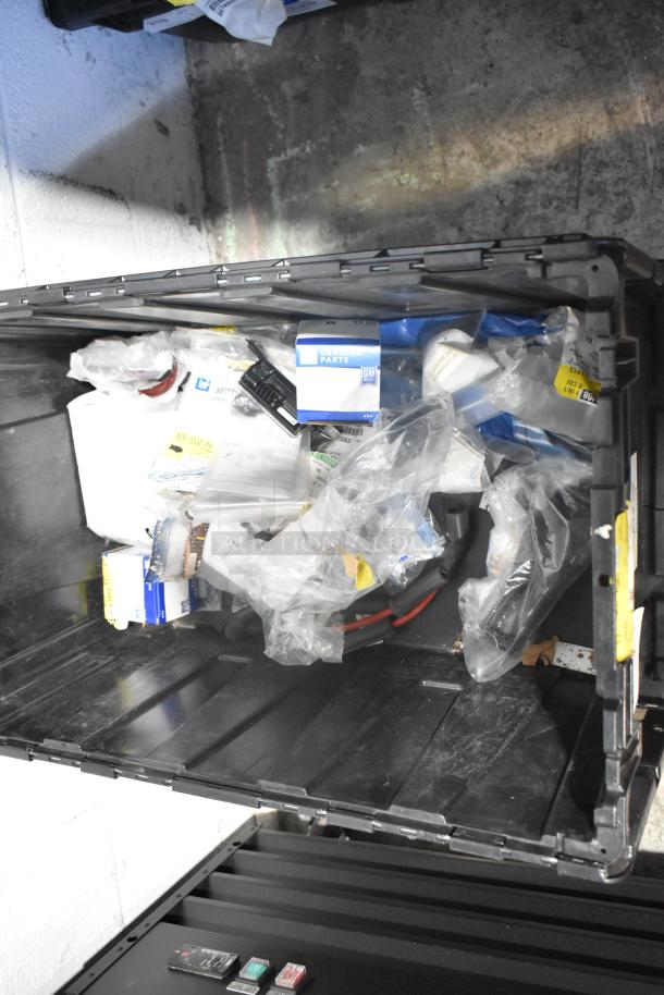 Brand new car parts lot in black poly bin, includes car mats, labeled GM Genuine Parts, various boxed and bagged items.