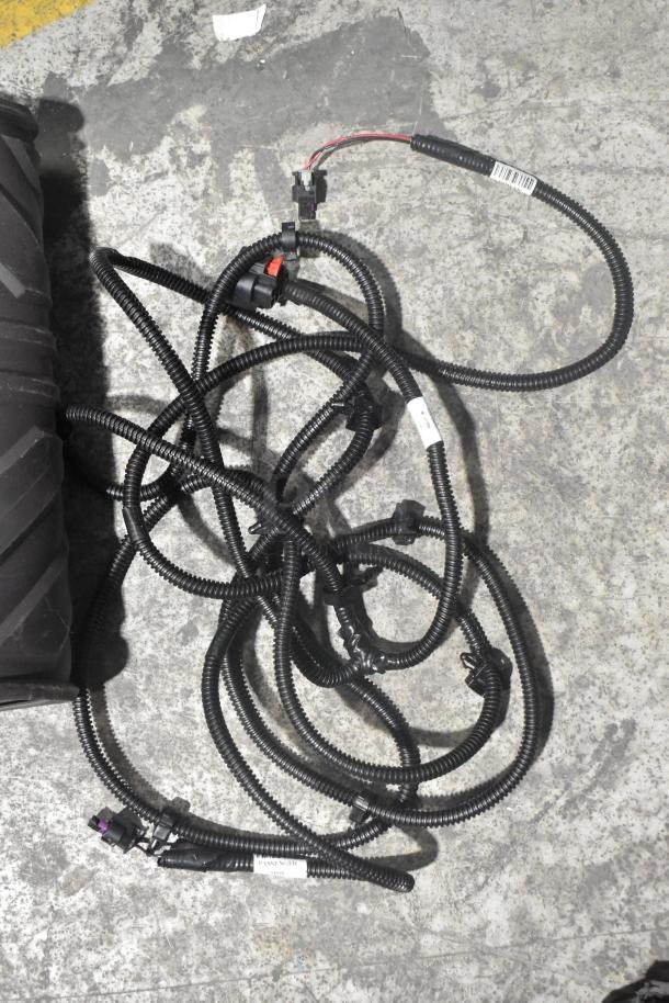 Brand new car parts lot, includes black wiring harness, labels visible, and black car mats, in black poly bin.