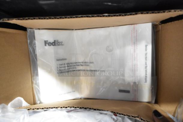 Brand new lot of various car parts, including emblems and pouches, packed in a black poly bin with FedEx pouch visible.