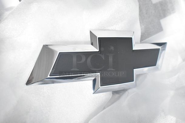 Car emblem with chrome finish, shown brand new in packaging.