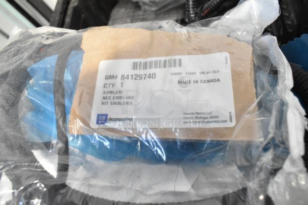 Brand new GM car parts, including handle and GM 84044906 brake deflector, in black poly bin. Labeled "Made in Canada".