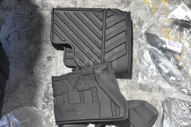Brand new black car mats with textured patterns, part of a lot of various car parts in poly bin, labels visible.