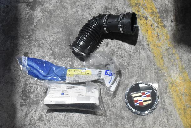 Brand new car parts including an air intake hose, emblem, and packaged accessories on a concrete floor.