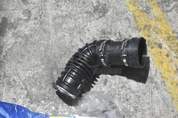 Brand new black car air intake hose with clamps, on concrete surface. Part of various car parts lot in black poly bin.