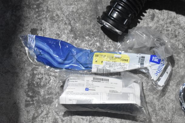 Lot of new car parts including GM accessories, car mats, emblem, and parts in a black poly bin.