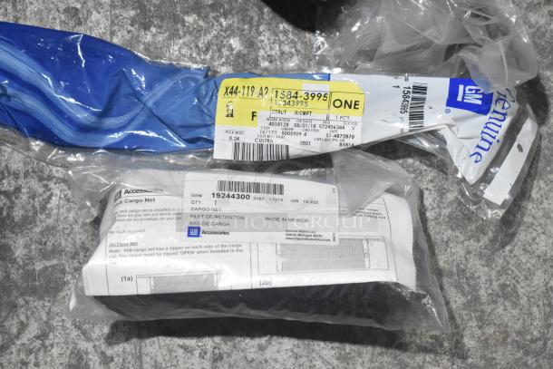 Brand new GM car parts and accessories in packaging, including a cargo net with labels and blue fabric item.