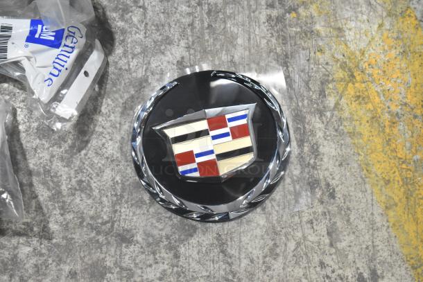Brand new Cadillac emblem on black surface, next to GM-labeled genuine car part packaging, indicating authenticity.