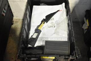 New car parts lot with mats, emblem, and items in black poly bin. Tags with barcodes and labels visible, indicating brand and specs.