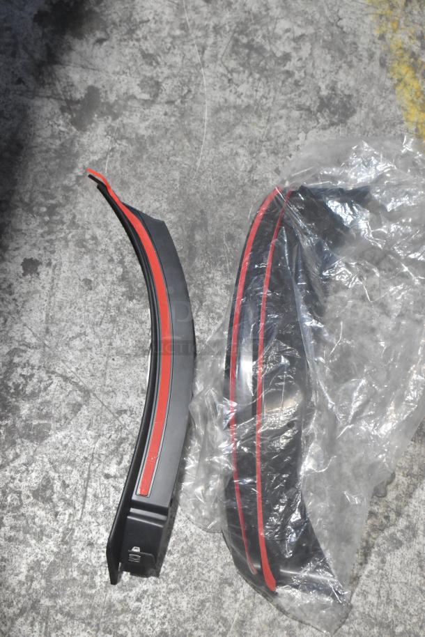 Brand new car parts including two curved pieces with red trim, partially wrapped in plastic, in a black poly bin.