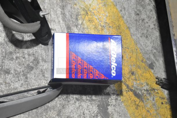 Brand new ACDelco car part box on a concrete floor, near black poly bin containing additional car parts.
