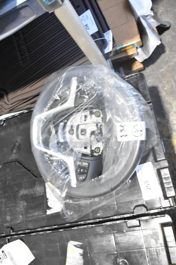 Lot of various brand new car parts, including steering wheel and black car mats, in a black poly bin with labels.