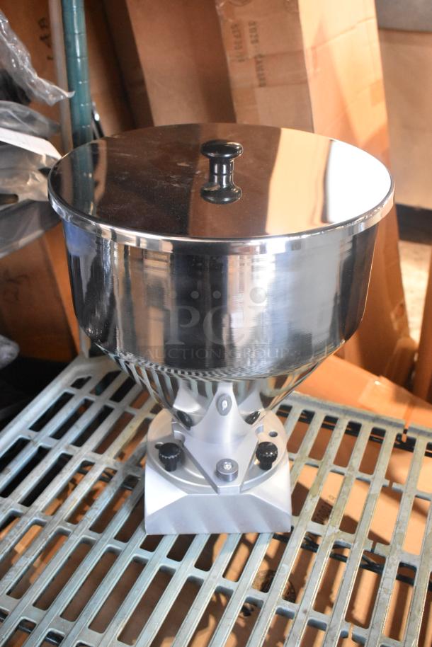 Shiny metal hopper with lid and knobs, in excellent condition, on a gridded metal shelf.