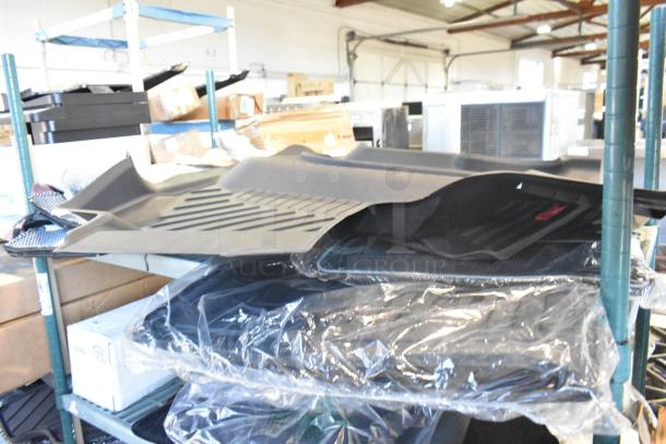 Two-tier lot of brand new items, including car mats, stacked on a shelving unit. Mats are black and gray, wrapped in plastic.