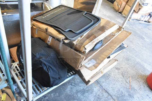Two-tier lot of brand new items including black car mats labeled "Camaro," stacked on boxes.