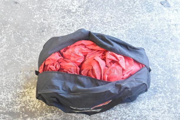 Black bag filled with red items, possibly car mats, zipper open, on a textured floor surface.