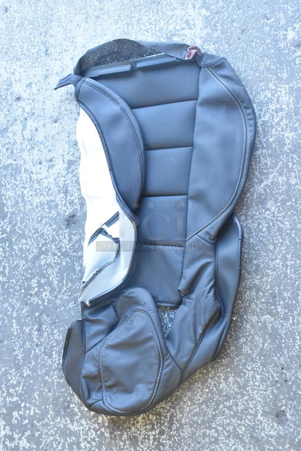 Brand new black car seat cover with textured panels, displayed on a concrete surface.