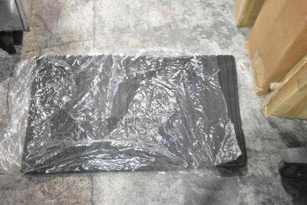 Brand new tier lot including car mats wrapped in plastic, on concrete floor. Appears to be unused.