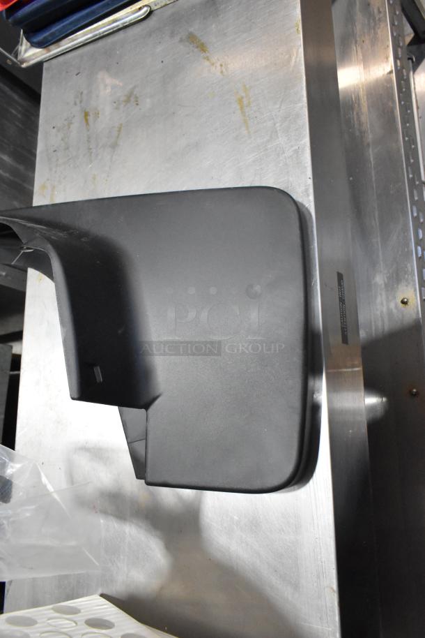 A brand new black plastic automotive part, likely a mud flap or guard, on a metal surface.