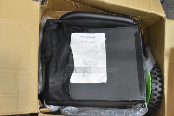 Brand new hand lawn mower in a box with assembly instructions. Features black handle and green wheels.
