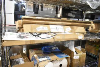 New scratch and dent items on shelves, including faucet, curved rod, cordless bamboo shades, and solar items. Labeled boxes.