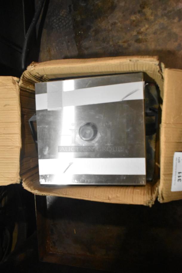 Brand new metal bin with scratches and dents, partially packaged in a cardboard box. Features a reflective surface and lid.