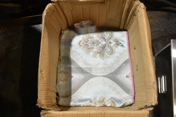 Cardboard box holding a metallic bin with decorative etching. Item is brand new with visible minor scratches and dents.