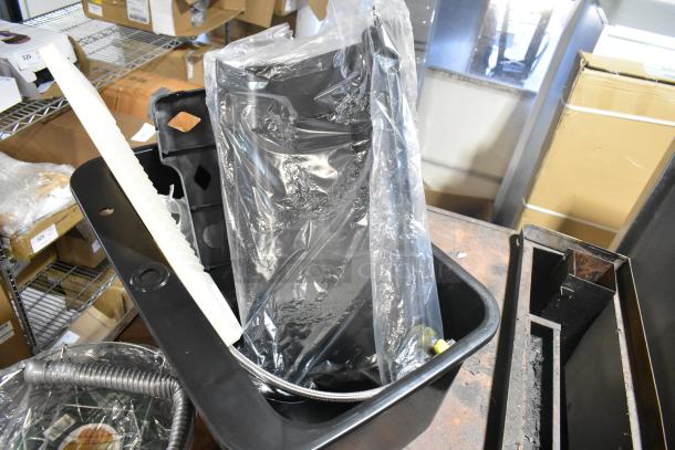 Brand new black poly bin with visible scratches and dents, containing assorted wrapped contents.