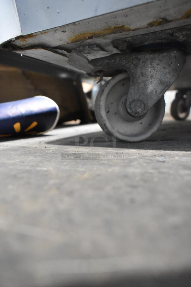 Metal freezer merchandiser with worn commercial casters, showcasing mild rust and wear, suitable for commercial use.