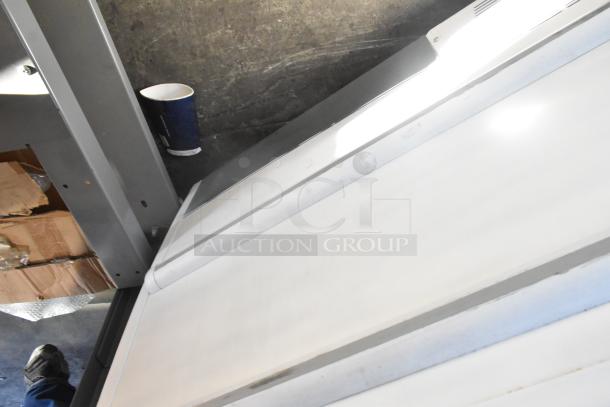 Metal commercial freezer merchandiser on casters, in used condition, located in a storage area with visible packaging materials.