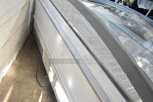 Metal commercial freezer merchandiser on casters, features glass top, white exterior, visible ventilation grille, and power cord.